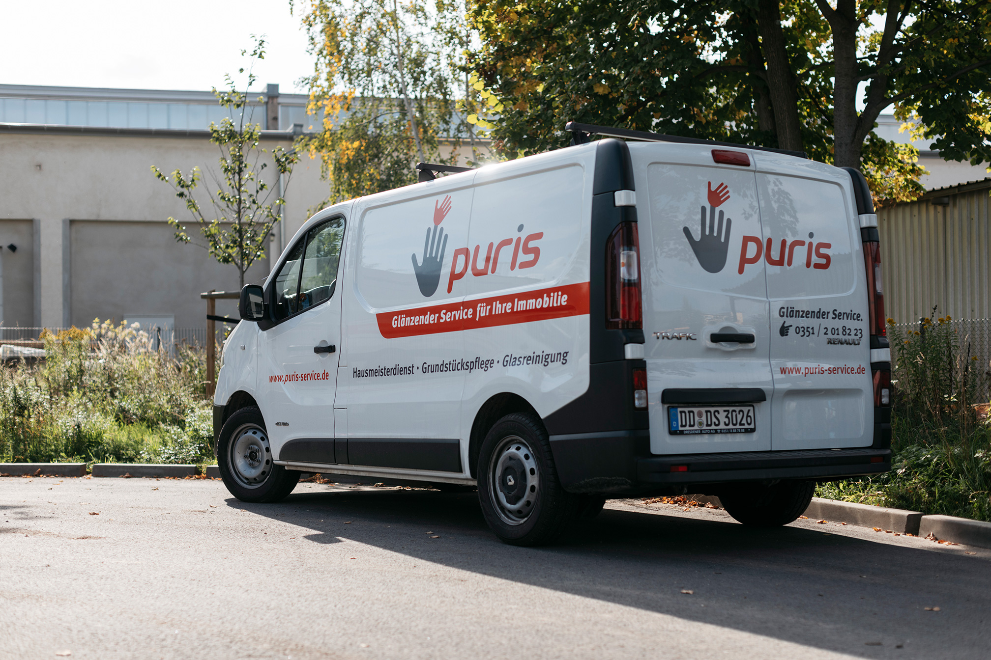 Ein weißer puris Firmenwagen mit dem puris-Logo und dem Slogan „Glänzender Service für Ihre Immobilie" steht auf einem Parkplatz in Dresden – auf der Seite sind die Leistungen Hausmeisterdienst, Grundstückspflege und Glasreinigung aufgeführt.