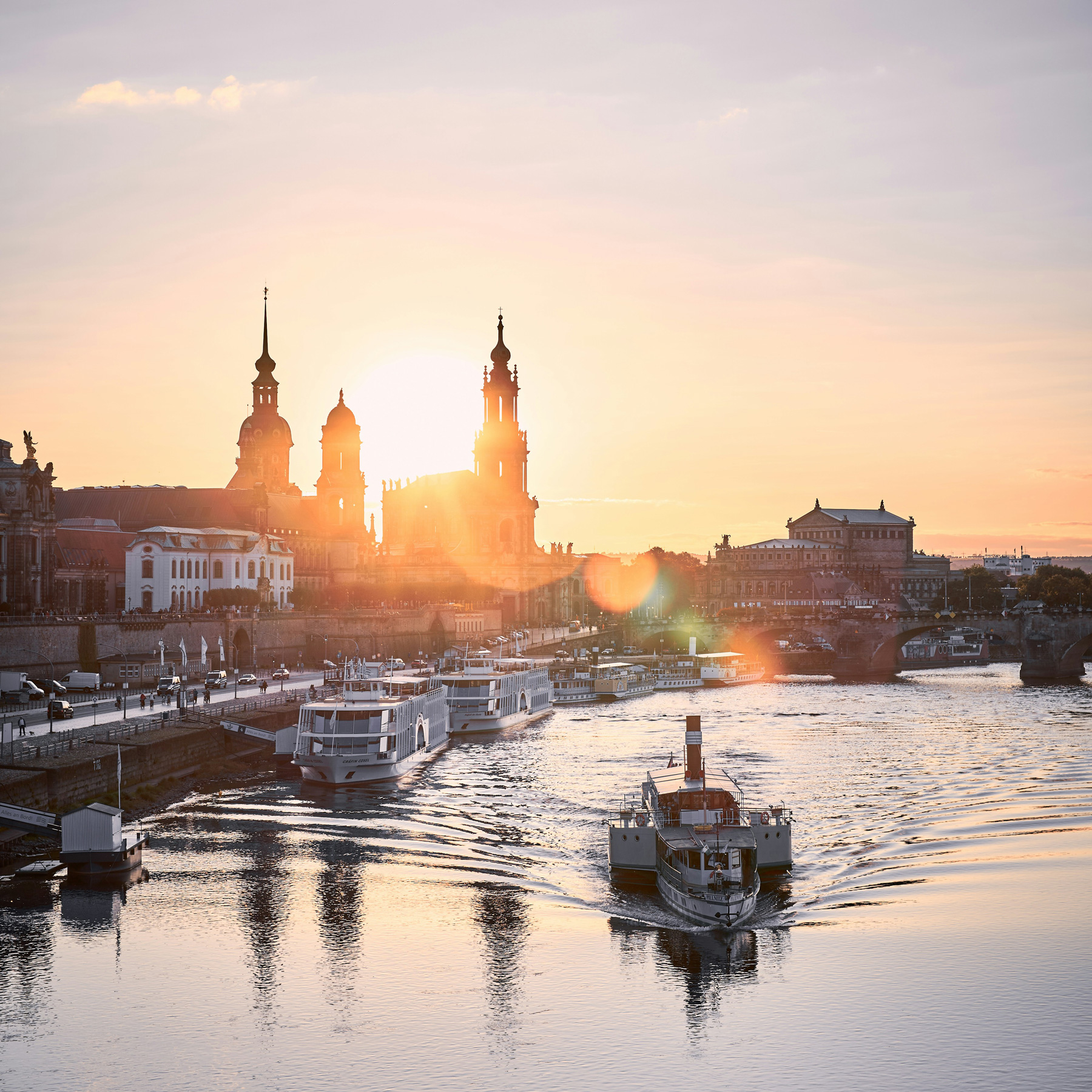 Dresden, Hauptsitz der puris Haushalts- und Unterhaltsreinigung, bei Sonnenuntergang über der Altstadt mit Blick auf die Elbe – im Vordergrund fährt ein historisches Dampfschiff flussaufwärts, im Hintergrund sind die Silhouetten der Hofkirche und der Semperoper zu sehen.